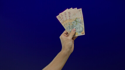 Man holding romanian lei banknotes against a blue background with focus on currency and hand...