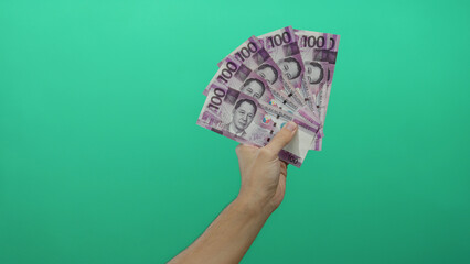 Caucasian man holding philippine pesos over vivid green wall, highlighting vibrant currency against...