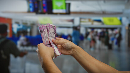 Man holding philippine pesos indoors at airport terminal showcasing travel finances amidst bustling...