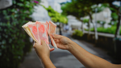 Man holding philippine pesos in an outdoor urban park setting, illustrating investment and business...