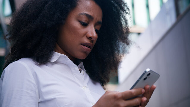 Frustrated African American woman female holding mobile phone smartphone sad entrepreneur businesswoman business displeased girl chat downtown city problem online bad news message technology manager