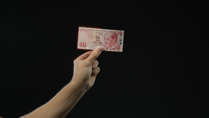 Man holding turkish lira banknote in hand against black isolated background, highlighting currency...