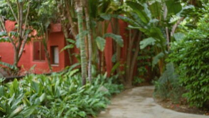 Blurred pathway in a tropical luxury resort surrounded by lush greenery and a vibrant red building, creating a serene and tranquil outdoor atmosphere.