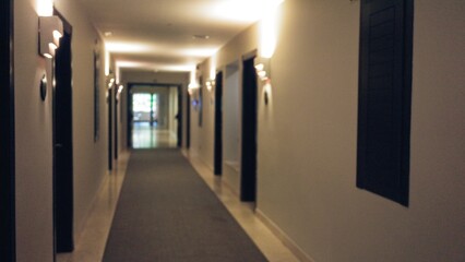 Defocused view of a dimly lit hotel corridor with blurred walls creating a serene, quiet atmosphere, featuring elegant lighting and a soft carpeted floor.