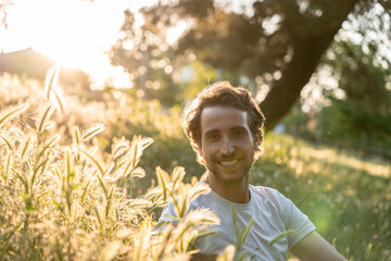 Relaxed man smiling under warm sunset light outdoors with happy expression