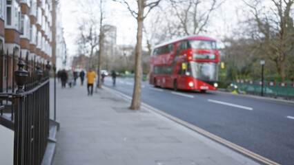 Naklejka premium Blurred red bus on london street in winter with people walking, capturing the essence of urban life in the uk amidst overcast skies.
