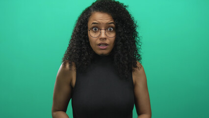 Young woman with curly hair and glasses wearing a black sleeveless top grasps her throat in studio;...