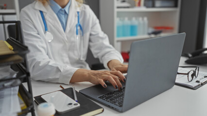 Middle-aged female doctor working on a laptop in a hospital room, focused on tasks with medical...