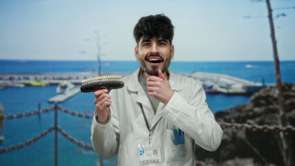 Young hispanic man in a lab coat examines dental tool against seaside port backdrop with boats and...