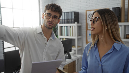 Man and woman discussing work in an office, showcasing teamwork in a modern workplace setting with...