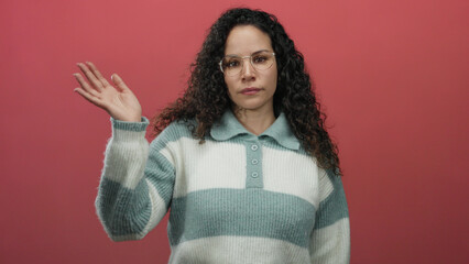 Woman with glasses waving over isolated pink background wearing a cozy striped sweater while...