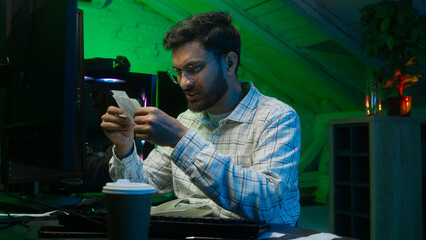 Frustrated Arabian Indian man programmer holding paper code bills problem checking information data...