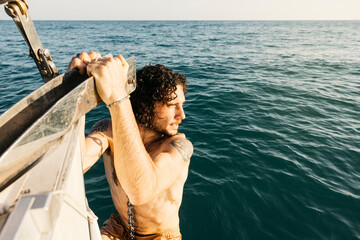 Sailor pulling up anchor on sailboat in ocean, enjoying his vacation