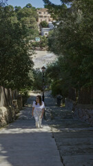 Woman walking up stone steps surrounded by lush greenery at beach in santanyi, mallorca with sea view in the background, capturing mediterranean essence.