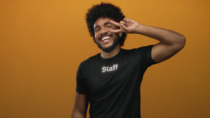 Man smiling in staff uniform against vibrant orange wall, expressing joy and positivity with a...