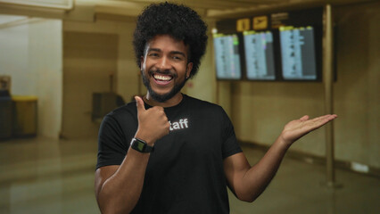 African american man in staff uniform at airport indoor pointing to flight information displays...
