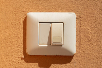 Old dirty light switch on orange wall in sunlight