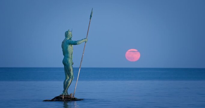 Statue of Neptune Holding Trident with Full Moon Twilight over sea horizon in the Background, beach resort complex St. St. Constantine and Helena, Varna, Bulgaria vertical