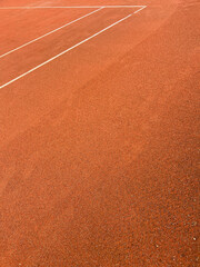 A close-up of a rain-moistened tennis court surface showing the distinctive brown gravel texture, with water droplets enhancing the natural clay material's rugged appearance.