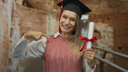 Young blonde woman wearing graduation cap and holding a diploma smiles in front of roman ruins,...