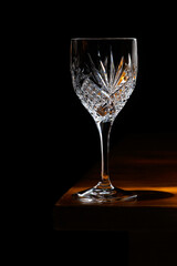 An empty crystal glass standing on the corner of a wooden table.