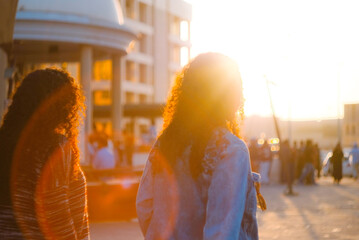 Two women walk through a sunlit city street at golden hour. A creative, dreamy concept to represent friendship, lesbian relationships, urban life.