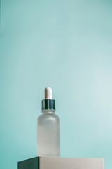 A frosted dropper bottle of facial serum is placed on a sculpted white pedestal with a soft teal...