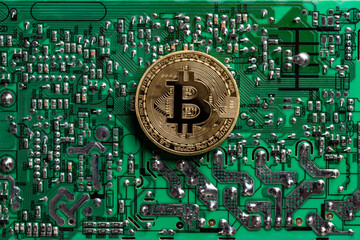 Golden coin with bitcoin symbol on a green printed circuit board with radio components on...