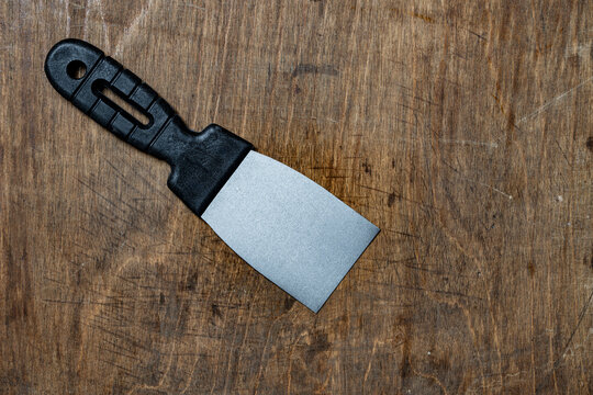 Putty spattle or putty knife with black handle and metal blade, ideal for spreading, scraping and smoothing putty or paint in painting and surface preparation task. Spatoula on wood board background