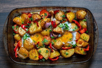 Baked vegetables with egg in a glass baking dish, top view, closeup. Potatoes, tomatoes, red pepper, onion and eggs baked in the oven. Simple rustic food from vegetables in summer