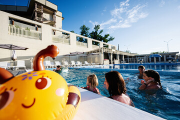 Families enjoying a sunny day swimming at a resort pool with vibrant float toys