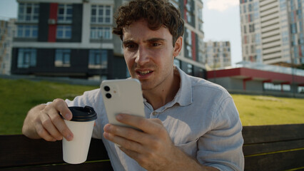Caucasian man drink coffee holding cup mobile phone smartphone bad news loss bet male guy...