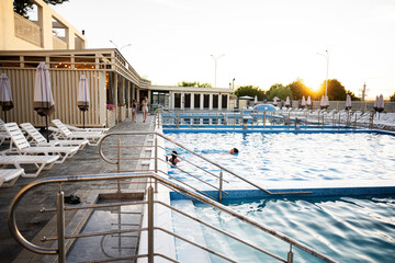 Outdoor swimming pool with lounge chairs and umbrellas under a serene sunset