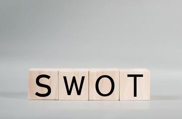 A wooden blocks with the word SWOT written on it on a gray background.
