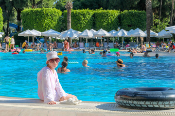 Kid girl sits by the pool with her feet in the water at the resort