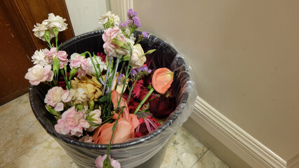 A bouquet of flowers in different varieties, thrown away into a rubbish bin. 
