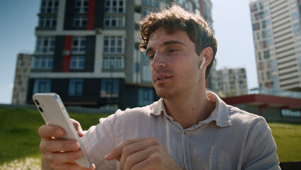 Caucasian man male guy sitting outside holding mobile phone smartphone technology device headphones...