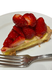 Closeup of delicious strawberry tart, served on a white plate with a fork.