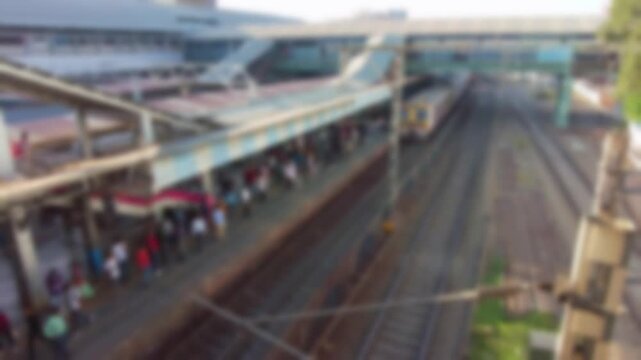 Bokeh local train departs from the platform of railway station. Blurry top angle view from the skywalk.