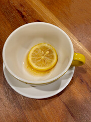 An empty tea cup with a slice of lemon and some leftover tea, on a wooden table.