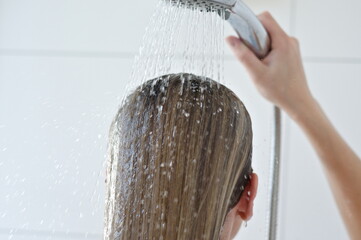 blond girl washes her hair with water in a shower on white background