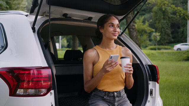 African American woman holding mobile phone smartphone chatting online trunk car auto automobile travel female girl outdoor cup coffee driver social media businesswoman business city texting tourist