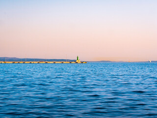 Obraz premium Split harbor in Croatia at sunset—featuring a tranquil breakwater and green lighthouse under a pastel sky, this serene coastal scene is perfect for travel and vacation inspiration.
