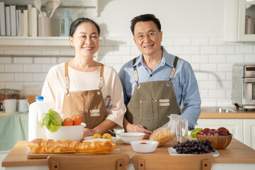 Portrait of Asian senior couple in apron cooking in the kitchen together and looking at camera