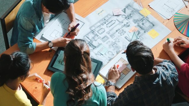 Top view of skilled civil engineer team writing at blueprint and planning design. Professional architect engineer working together sharing idea and taking a note in project plan at table. Symposium.