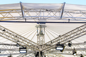 Central structure of a large outdoor canopy displaying metal framework and lights during an event setup in bright daylight