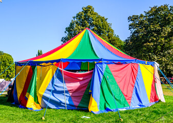 Brightly colored circus tent stands in a lively outdoor park on a sunny day with lush green grass and clear blue skies © fottoo