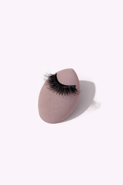 Makeup sponge with false eyelashes on light background