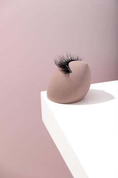 Makeup sponge with false eyelashes on pastel background