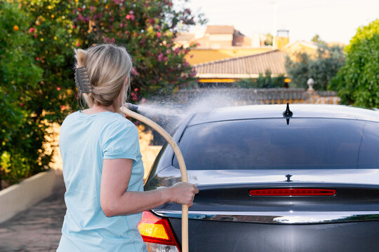 Woman cleaning car with hose on a sunny day
